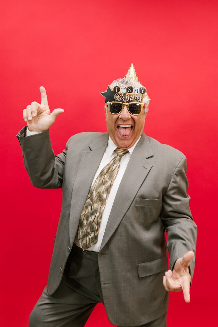 Elderly man in a suit joyfully celebrating his birthday with a red background.